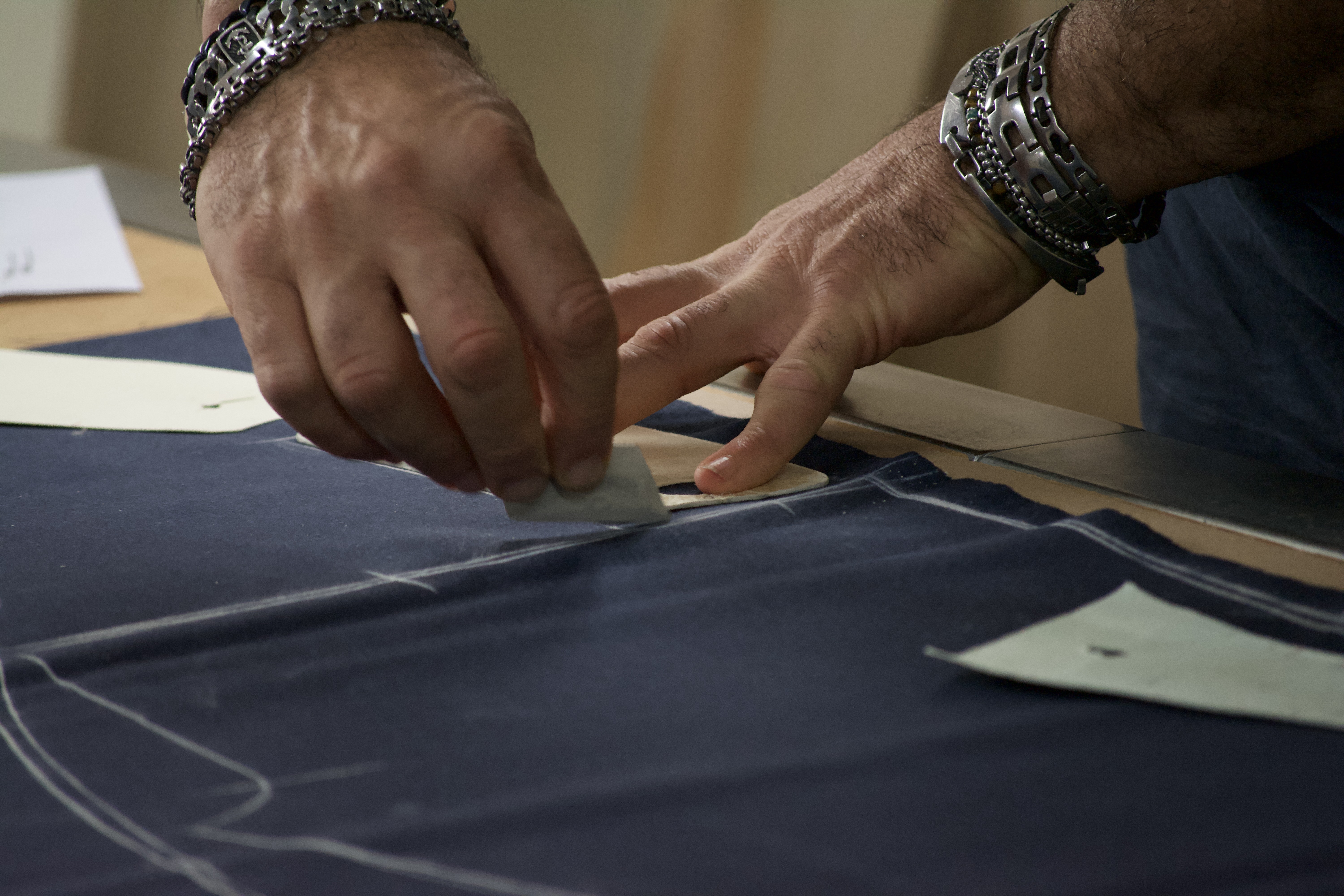 A craftsman marking pattern lines onto fabric with chalk at the cutting table